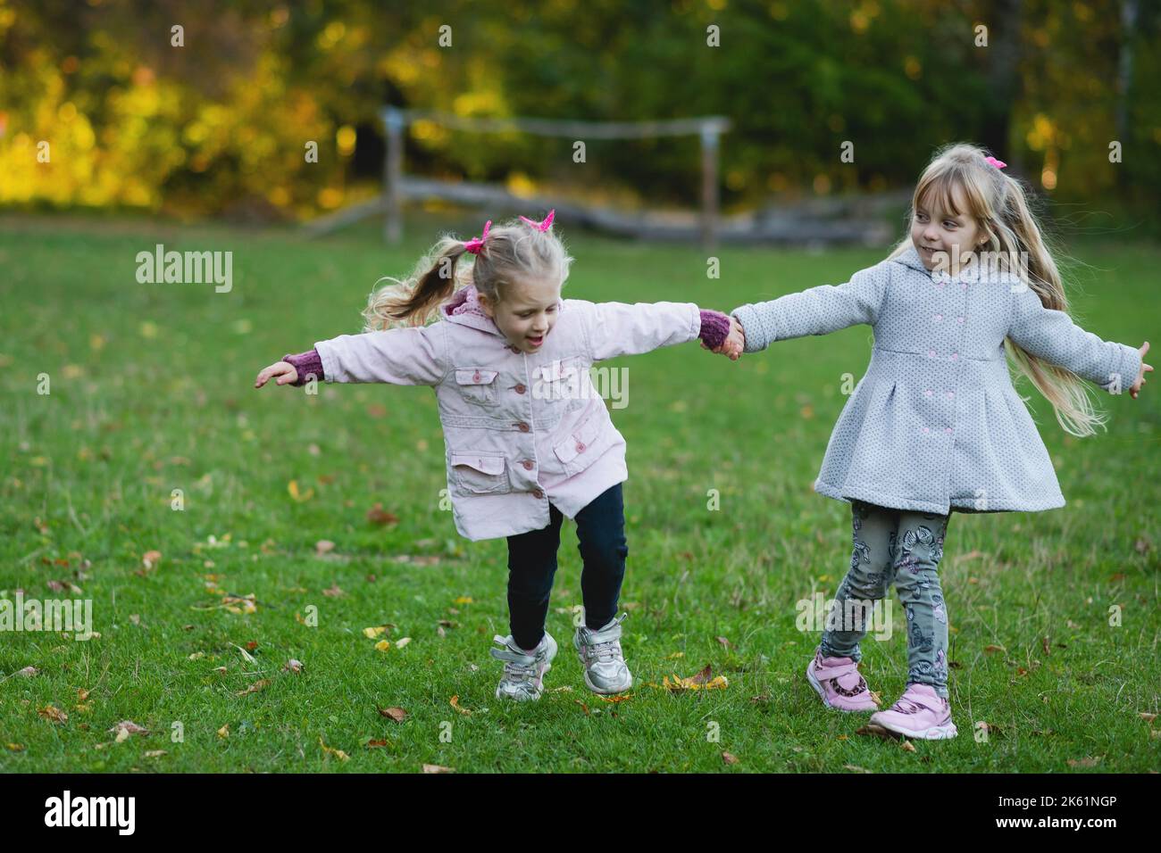 Two child girls play on the lawn in the autumn park. Girls run and spin ...