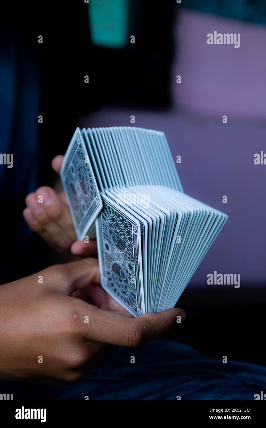 A vertical shot of hands doing a trick with a set of poker cards with a purple background. Stock Photo