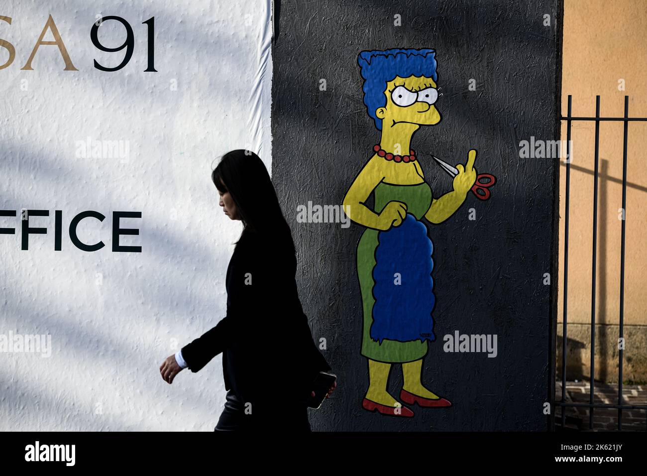 Milan, Italy. 11th Oct, 2022. Milan, Italy - October 11, 2022: a woman walks past a mural entitled ‘The Cut 2' by street artist aleXsandro Palombo depicting The Simpsons' character Marge Simpson cutting her hair and giving the middle finger in solidarity with the women of Iran in front of the Iranian Consulate. A first version of a similar mural, entitled 'The Cut' appeared on October 5 at the same location and was later on removed. (Photo by Piero Cruciatti/Sipa USA) Credit: Sipa USA/Alamy Live News Stock Photo