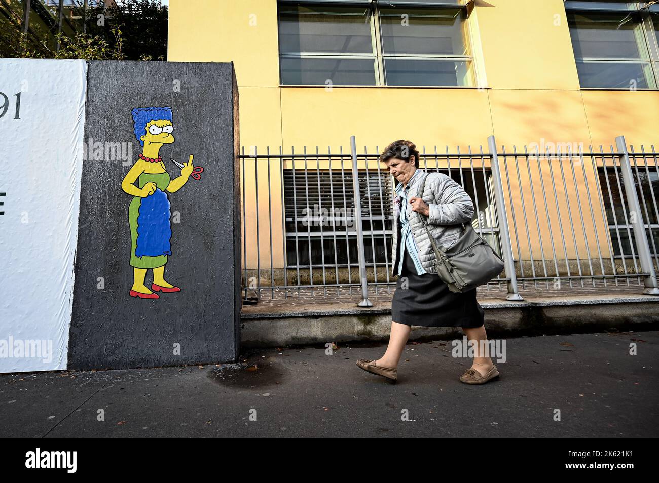 Milan, Italy. 11th Oct, 2022. Milan, Italy - October 11, 2022: A woman walks past a mural entitled ‘The Cut 2' by street artist aleXsandro Palombo depicting The Simpsons' character Marge Simpson cutting her hair and giving the middle finger in solidarity with the women of Iran in front of the Iranian Consulate. A first version of a similar mural, entitled 'The Cut' appeared on October 5 at the same location and was later on removed. (Photo by Piero Cruciatti/Sipa USA) Credit: Sipa USA/Alamy Live News Stock Photo