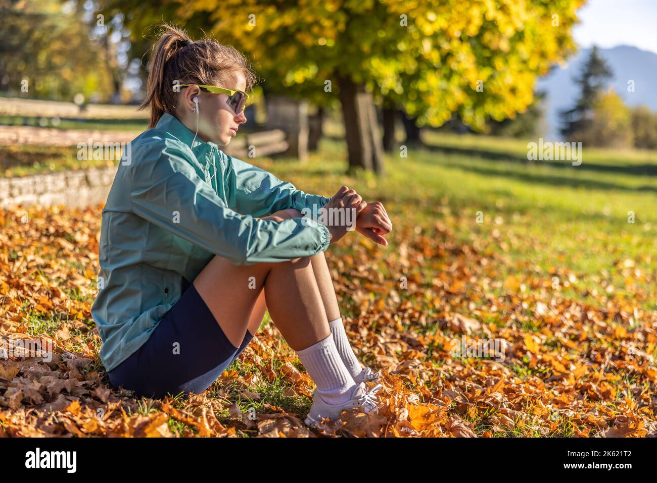 A young sportswoman rests after a run in the autumn leaves at sunset and checks her caloric