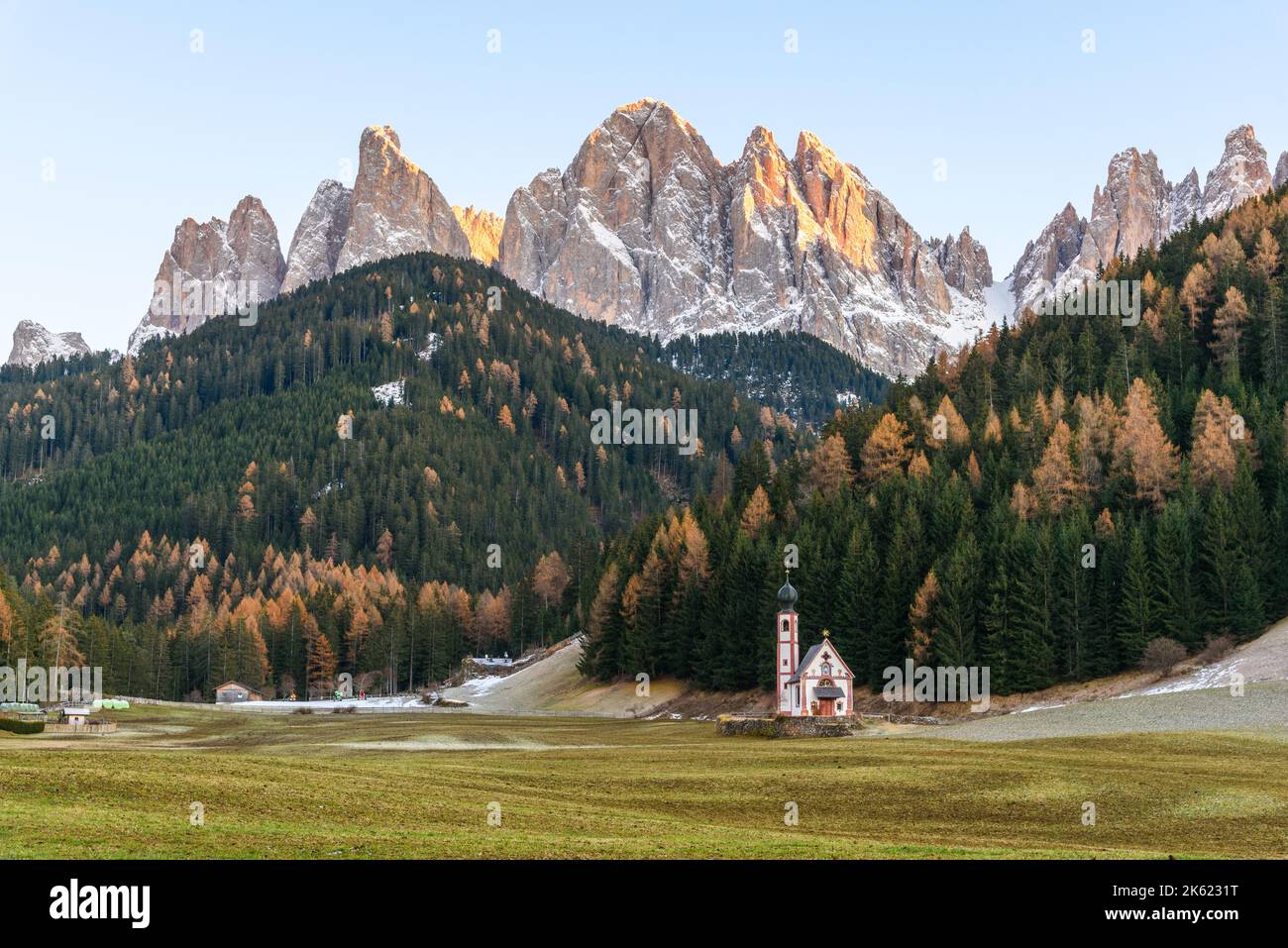 Autumnal sunset in the Dolomites. A lonely small church stands in the middle of a meadow at the foot of towering peaks. Stock Photo