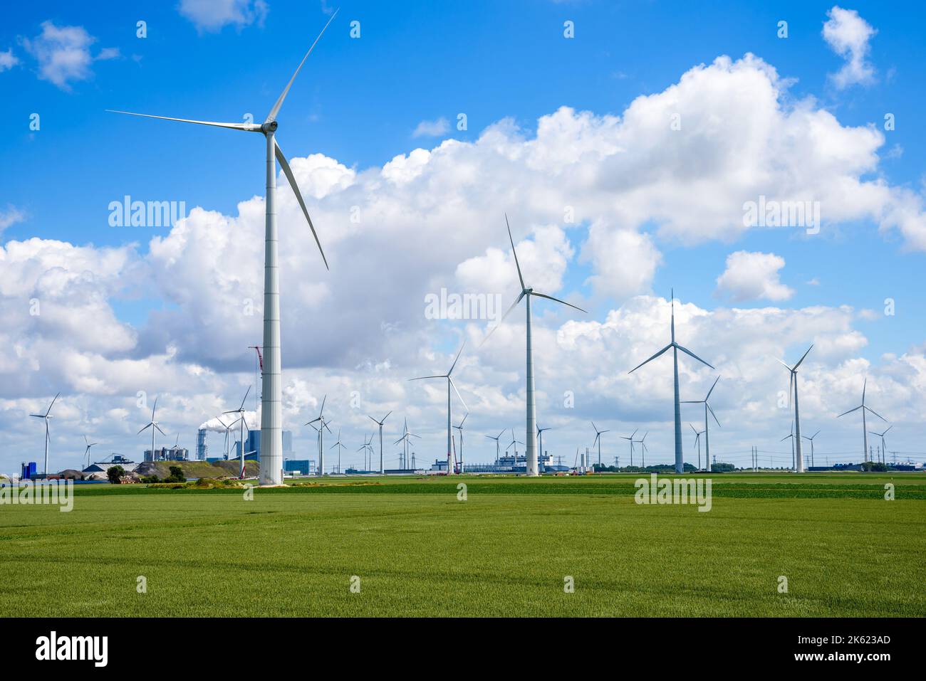 Wind farm in a field under blue sky with clouds. Coal-fired power plant is visible in background. Stock Photo