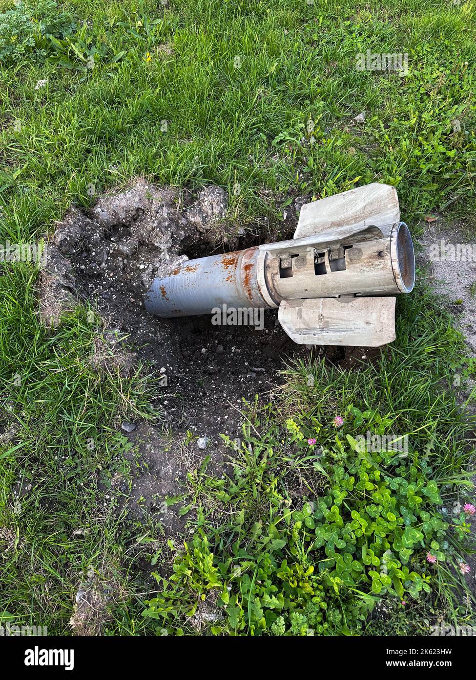 Russian MLRS Grad projectile in the ground next to grass on liberated from occupation territory of Ukraine. Result of Russian bombardment. Concept of Stock Photo