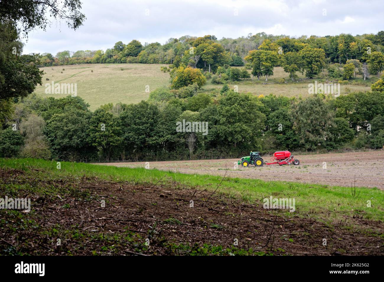 A green tractor with a red trailer working a field  in the Surrey Hill's at Abinger Roughs near Dorking on an autumn day England UK Stock Photo