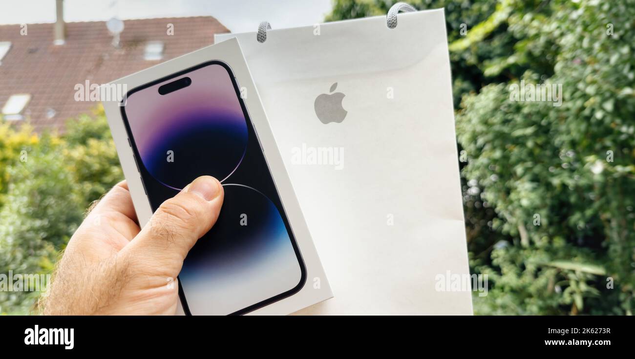 Paris France - Sep 18 2022: POV male hand holding new Apple Computers iphone 14 Pro cardboard box with present paper bag with iconic logotype - garden green background Stock Photo