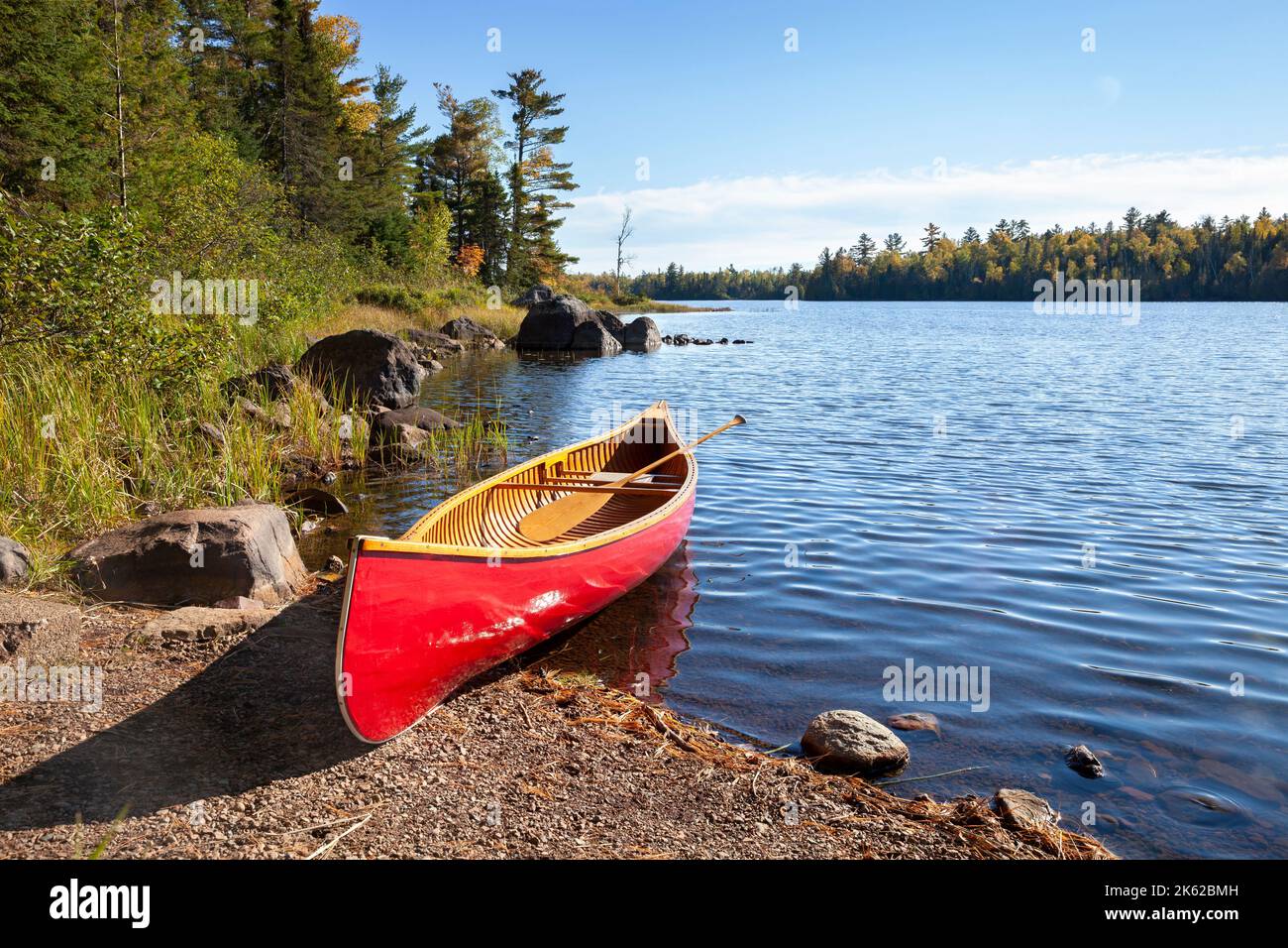 Red wooden canoe on shore of northern Minnesota lake with rocks and pines along the shore Stock Photo