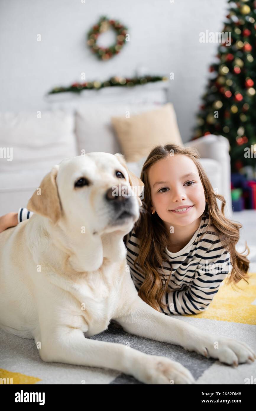 Smiling girl hugging labrador while lying on floor during new year ...