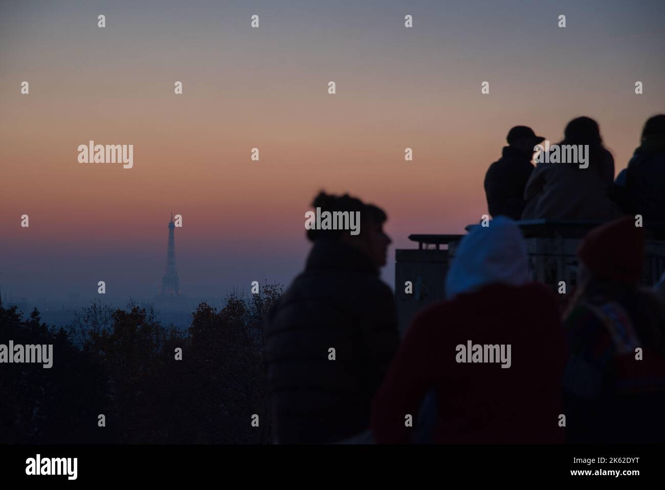 Young people admiring Parisian cityscape view with Eiffel tower at background at sunset and socializing. Belleville park in Paris, France. Stock Photo