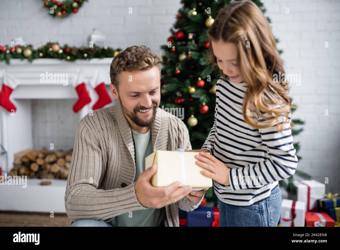Positive man in knitted cardigan holding gift box near child during ...
