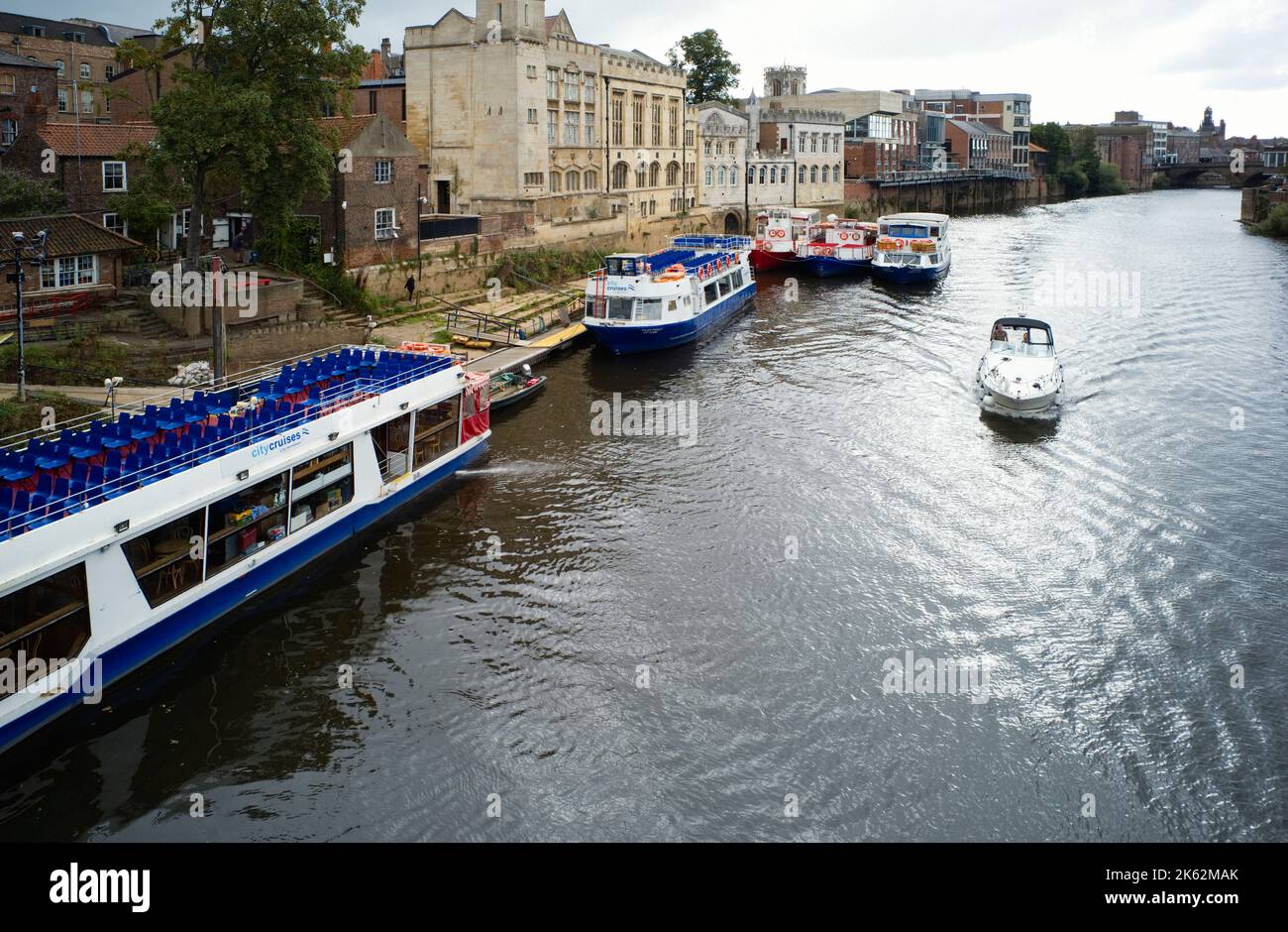 A small boat passes moored river trip boats on the river Ouse in York Stock Photo