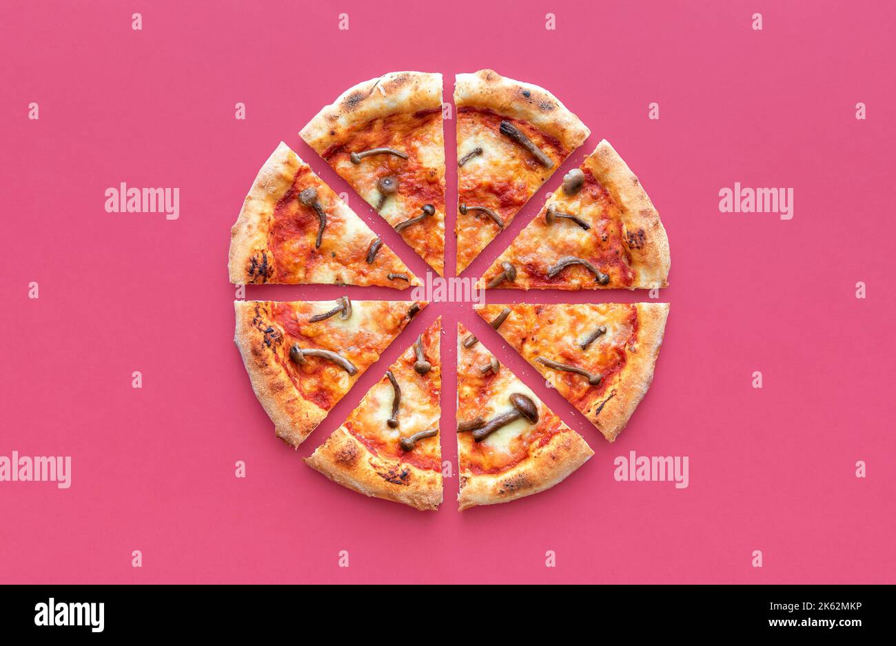 Above view with a sliced pizza isolated on a red-magenta table. Delicious homemade pizza with wild edible mushrooms. Stock Photo