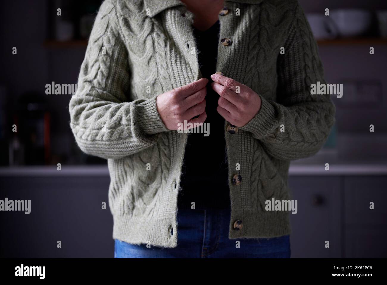 Woman Putting On Extra Jumper Clothing Trying To Keep Warm During Cost Of Living Energy Crisis Stock Photo