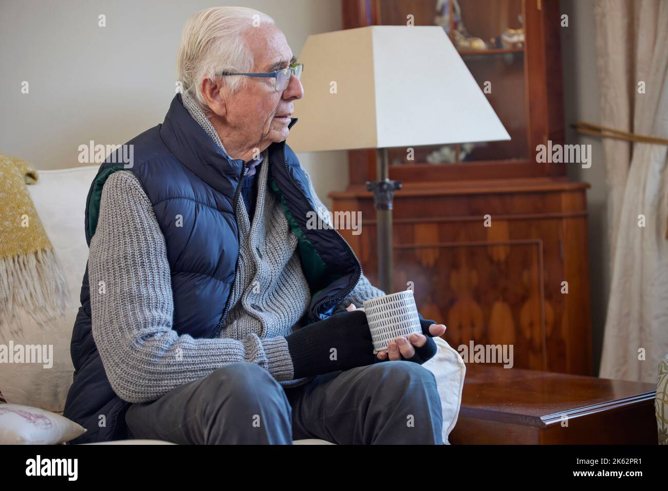 Senior Man Wearing Extra Clothes With Hot Drink Trying To Keep Warm At