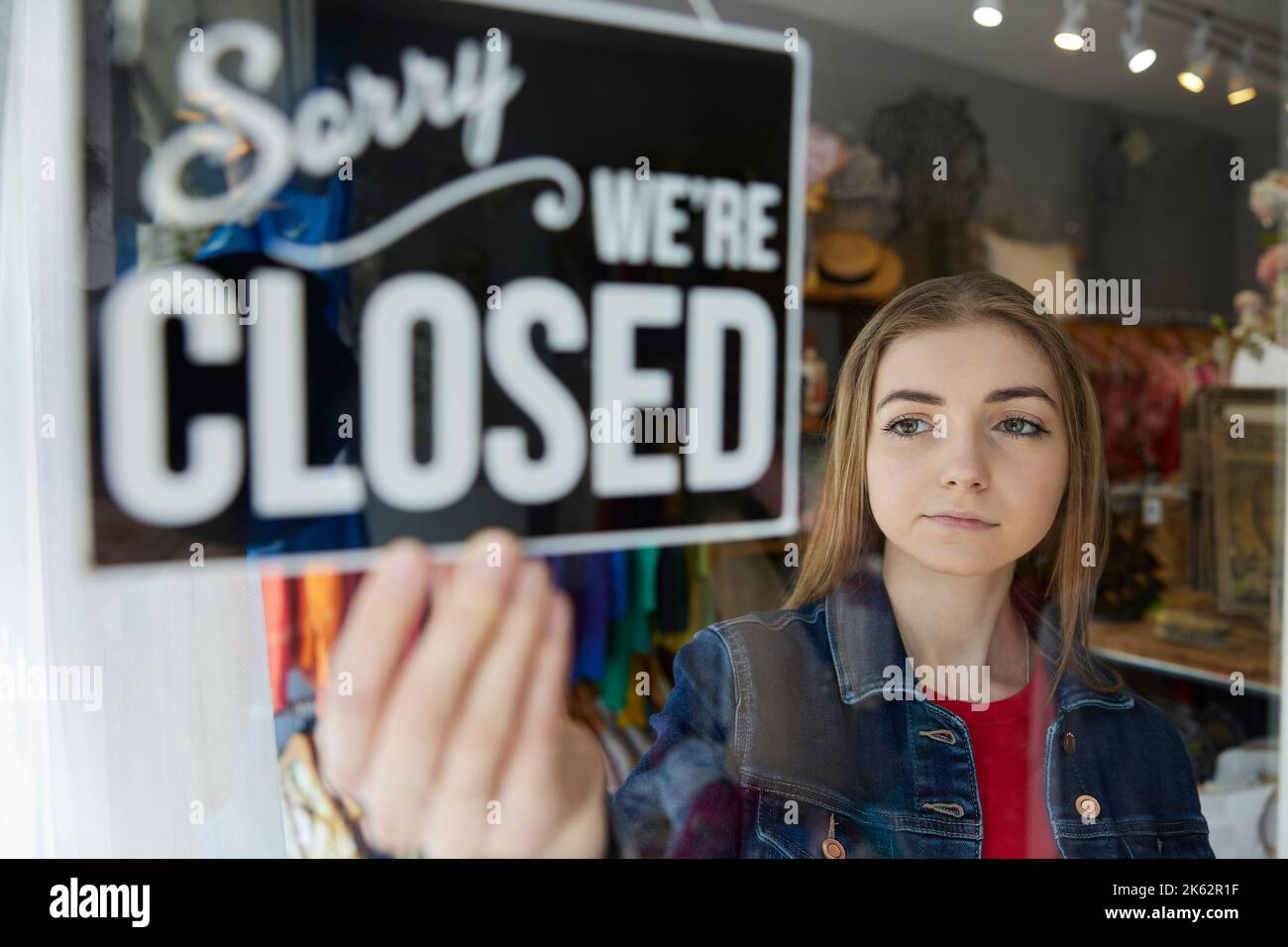 Sad Female Owner Of Small Business Turning Round Closed Sign In Shop Window Stock Photo