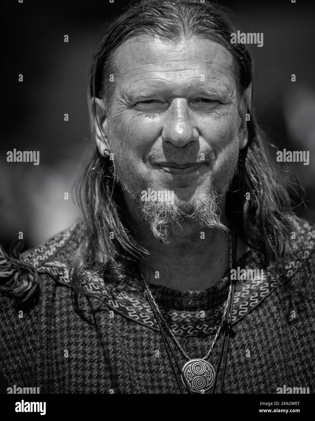 A vertical grayscale shot of a long-haired adult man wearing a medieval-styled jewelry Stock Photo