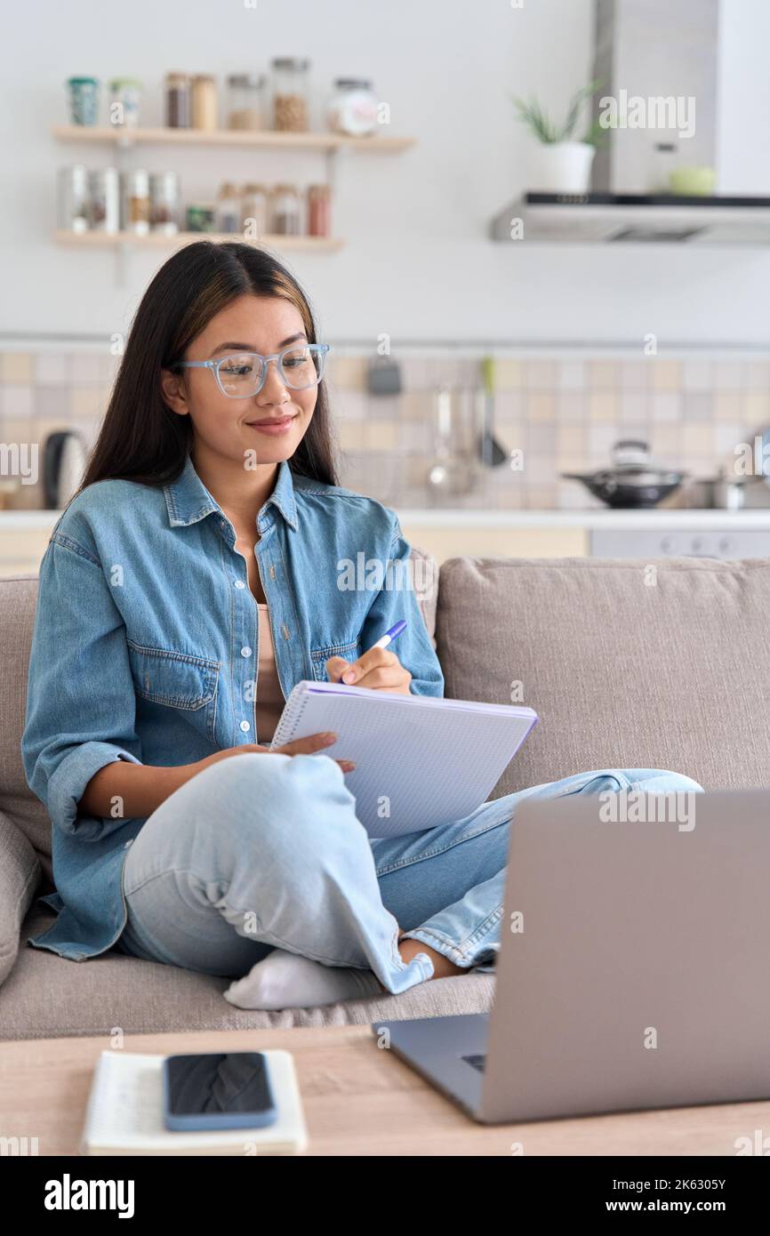 Teenager asian woman watching webinar on laptop making notes Stock Photo