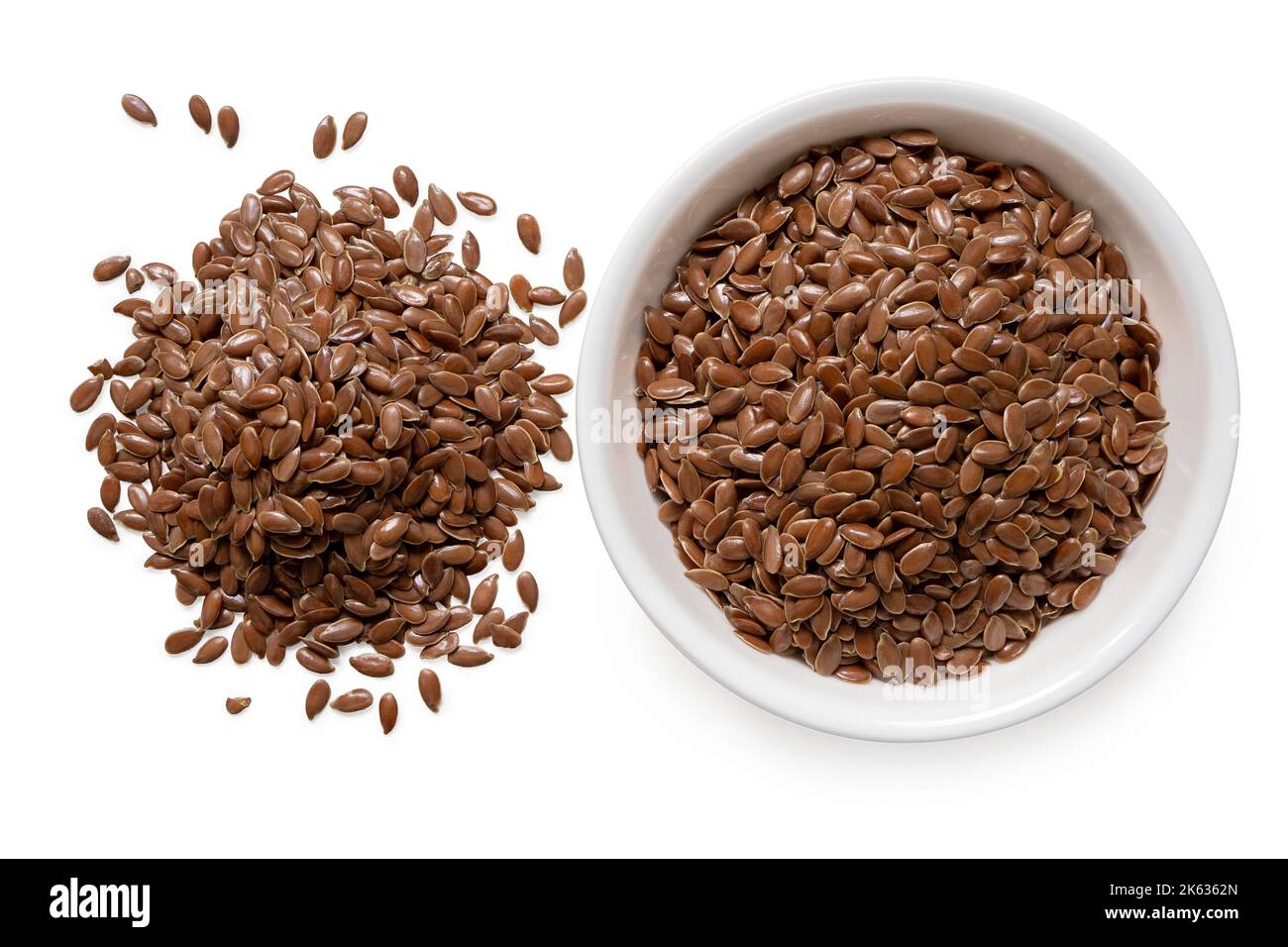 Flax seeds in a white ceramic bowl next to a pile of flax seeds isolated on white. Top view. Stock Photo
