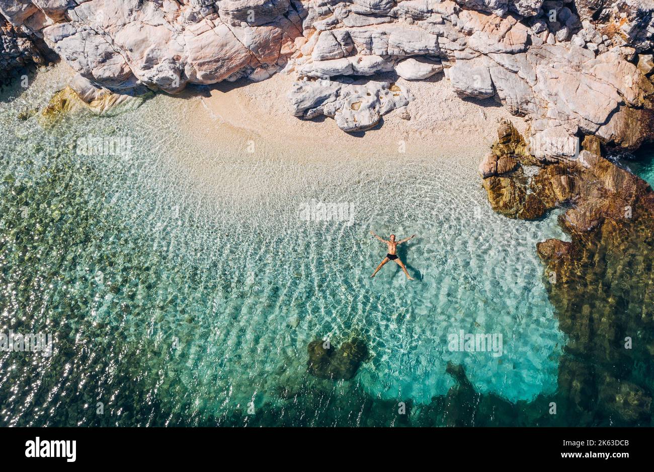 Aerial photo of man lying on the water in STAR pose on rocky pebbly