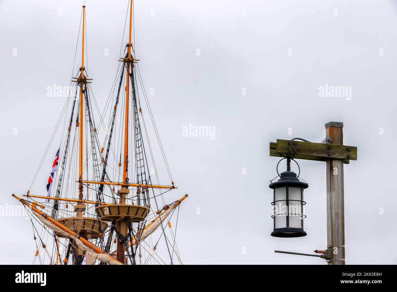 Top of a tall ship masts with a light post and hanging lantern in the foreground. Stock Photo