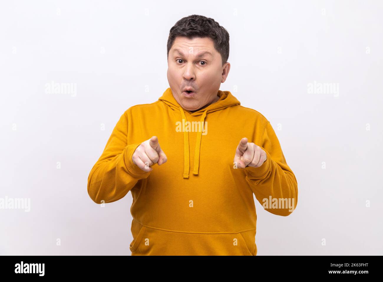 Portrait of astonished man points finger at camera and looking with shocked amazed expression, very surprised at something, wearing urban style hoodie. Indoor studio shot isolated on white background. Stock Photo