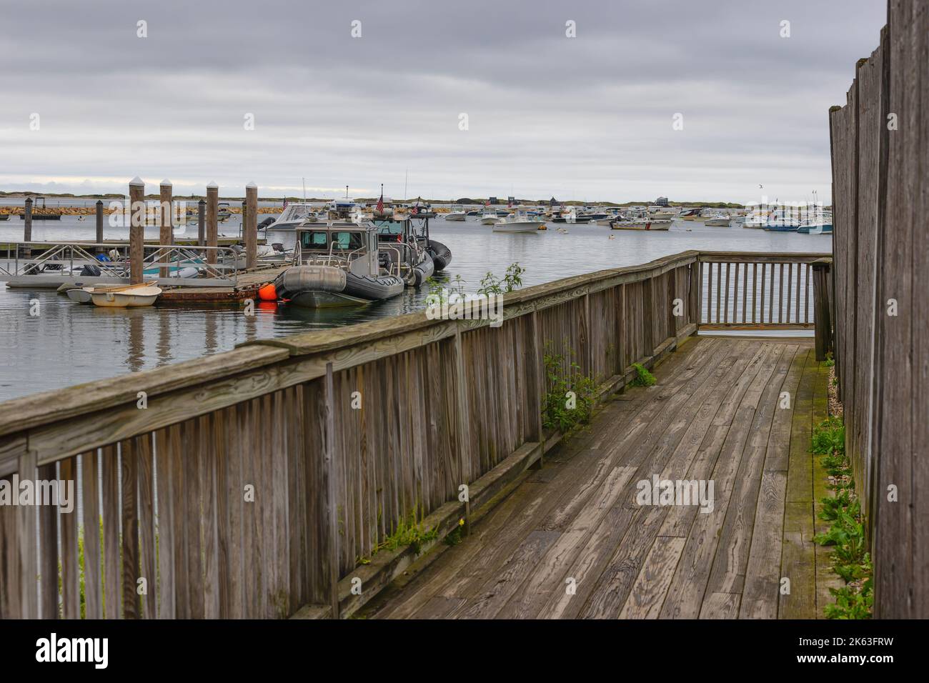 Plymouth, Massachusetts, USA - September 12, 2022: A wooden walkway next to a building overlooking Plymouth Harbor under cloudy skies. Stock Photo