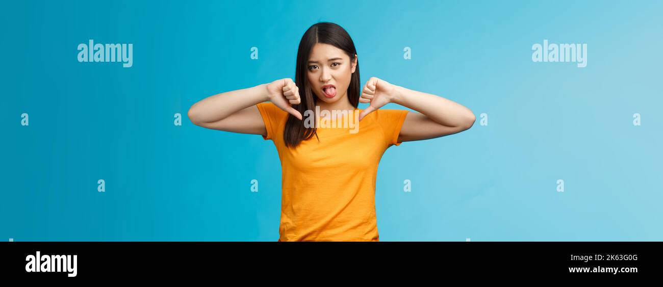 Disappointed upset and unimpressed cute childish asian girl dark haircut, frowning cringing dislike, aversion, show thumbs-down stick tongue disgust Stock Photo