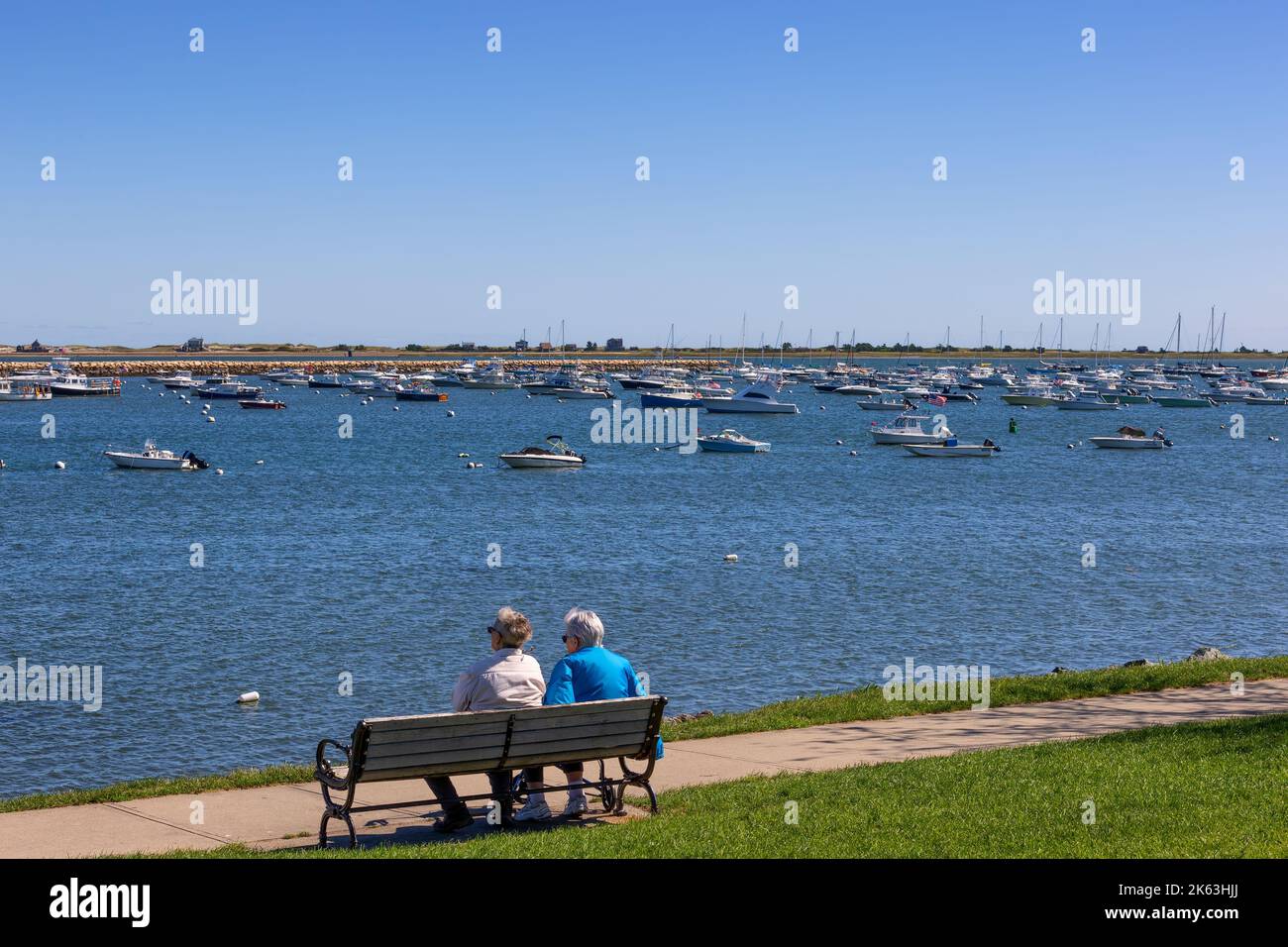 Plymouth, Massachusetts, USA - September 15, 2022: Two peope sit on a bench enjoying the view of the harbor on a sunny fall Day. Stock Photo