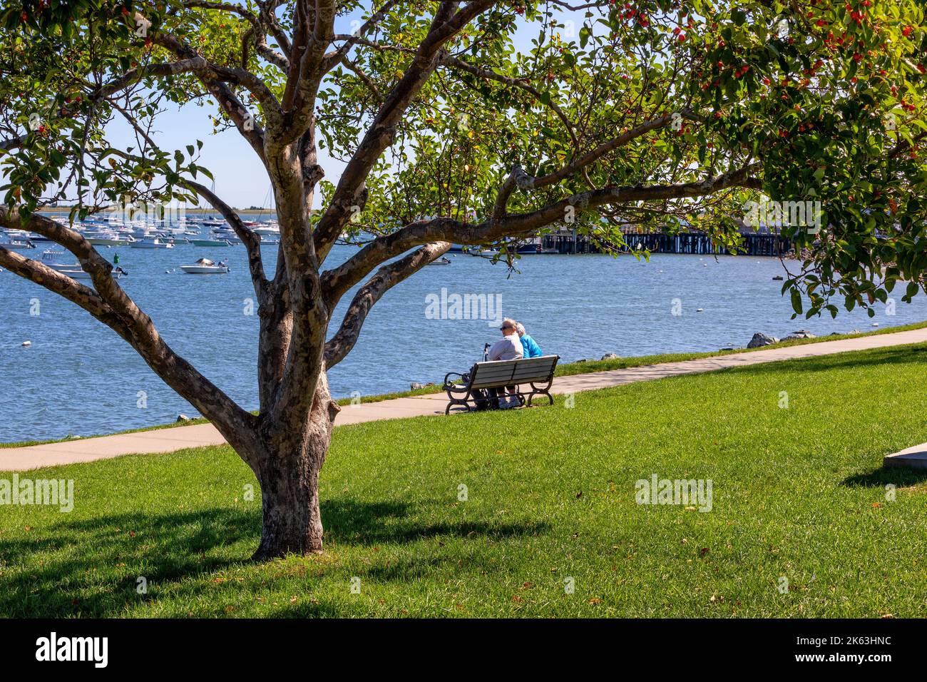 Plymouth, Massachusetts, USA - September 15, 2022: Two people sit on a bench enjoying the view of the harbor on a sunny fall day. Stock Photo