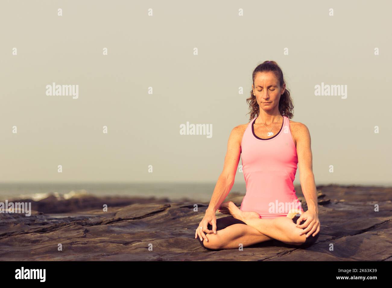 Young woman practicing yoga and meditation on the rocks by the sea in Vagator Beach, Goa, India. Relax, zen like, focus, self connection concept Stock Photo