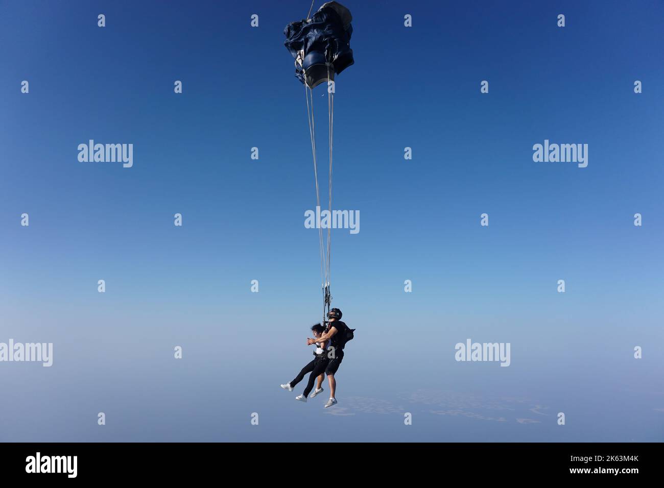 Dubai, United Arab Emirates: certified skydiving tandem instructor, with a beginner attached via harness, deploys the parachute midair to create drag. Stock Photo