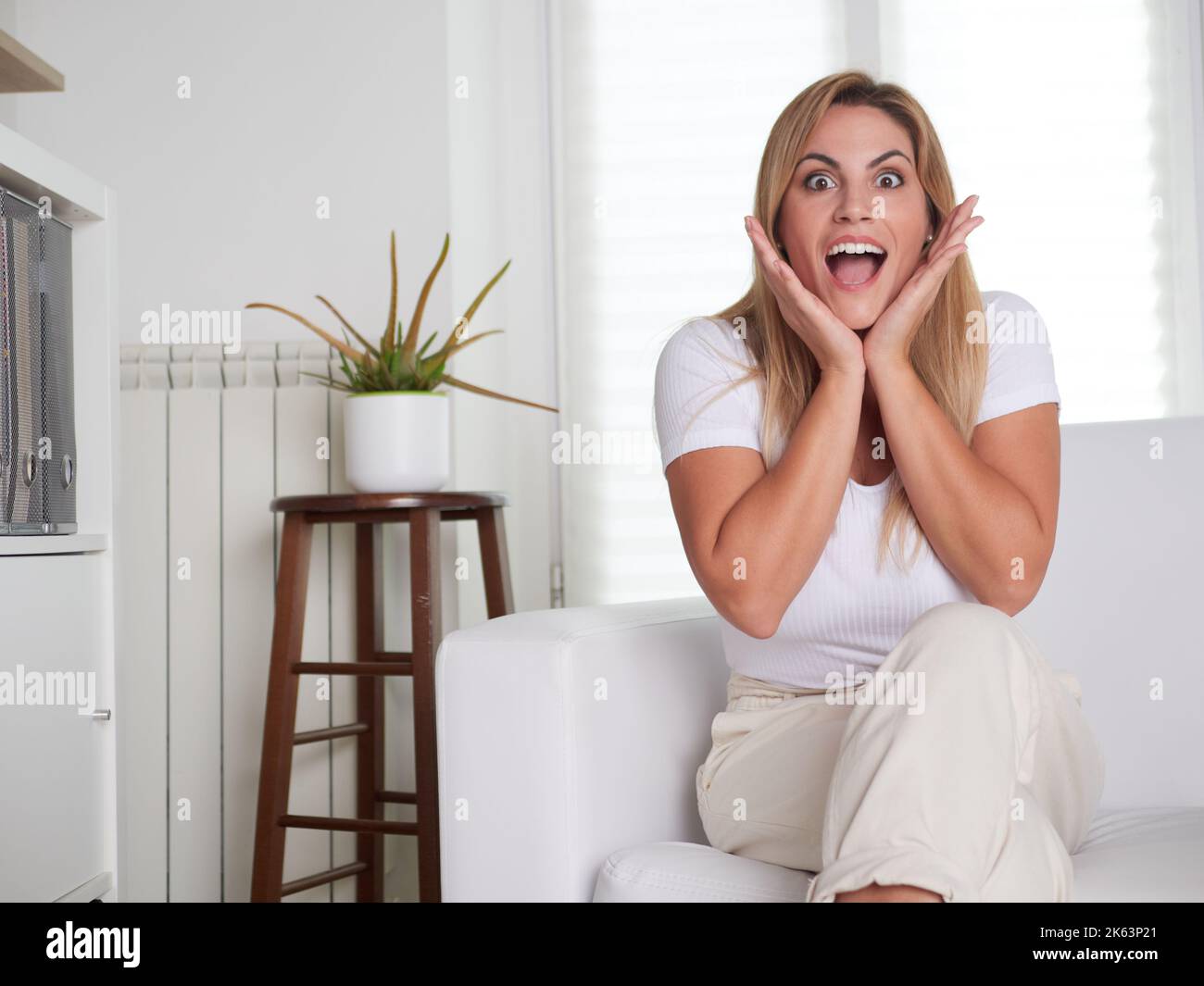 Carefree woman shocked sitting on a sofa at home Stock Photo