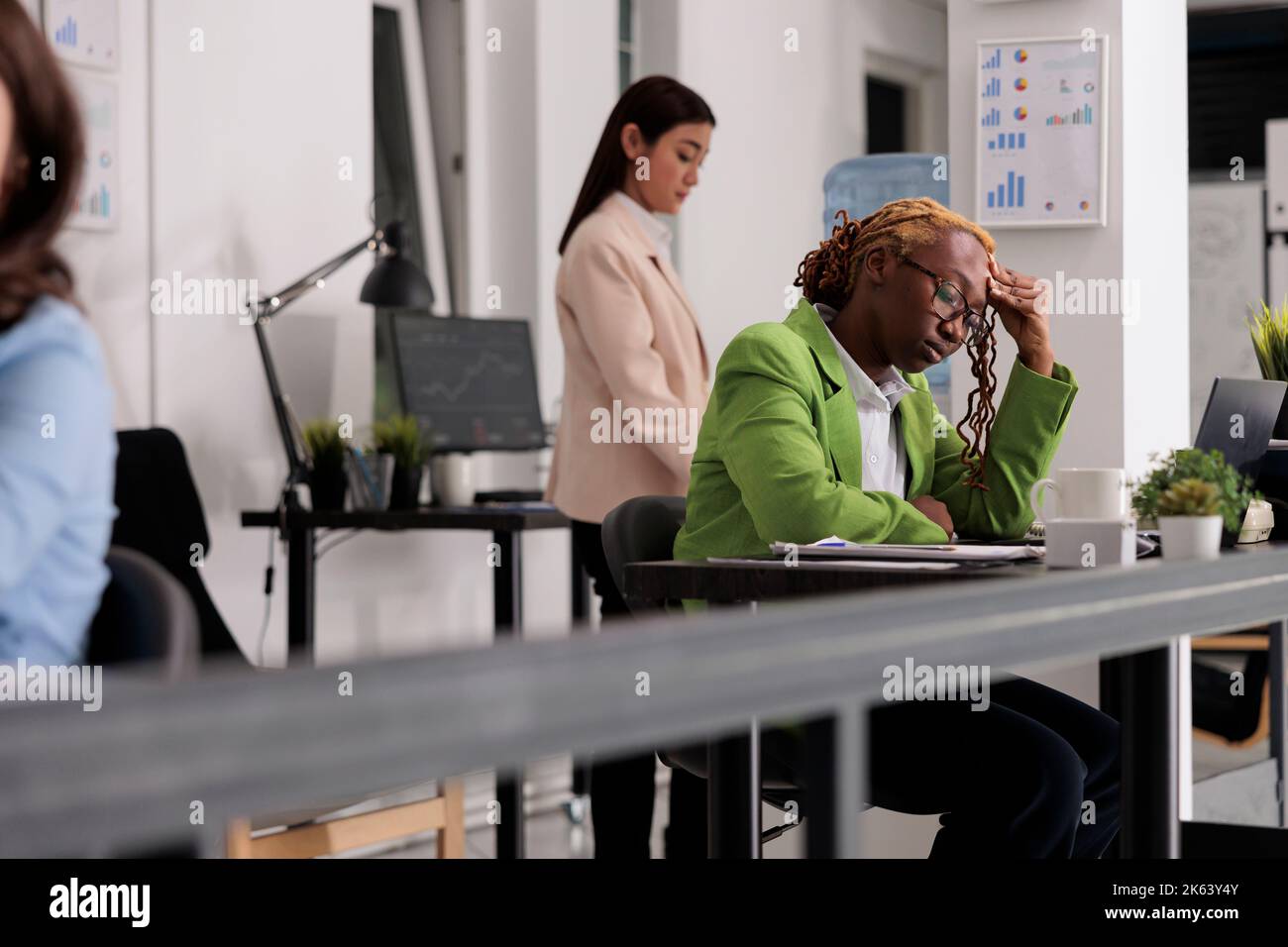 Sad employee having headache at work, touching forehead, exhausted woman in coworking space. Office worker suffering from migraine symptom, frustrated person feeling unwell at workplace Stock Photo