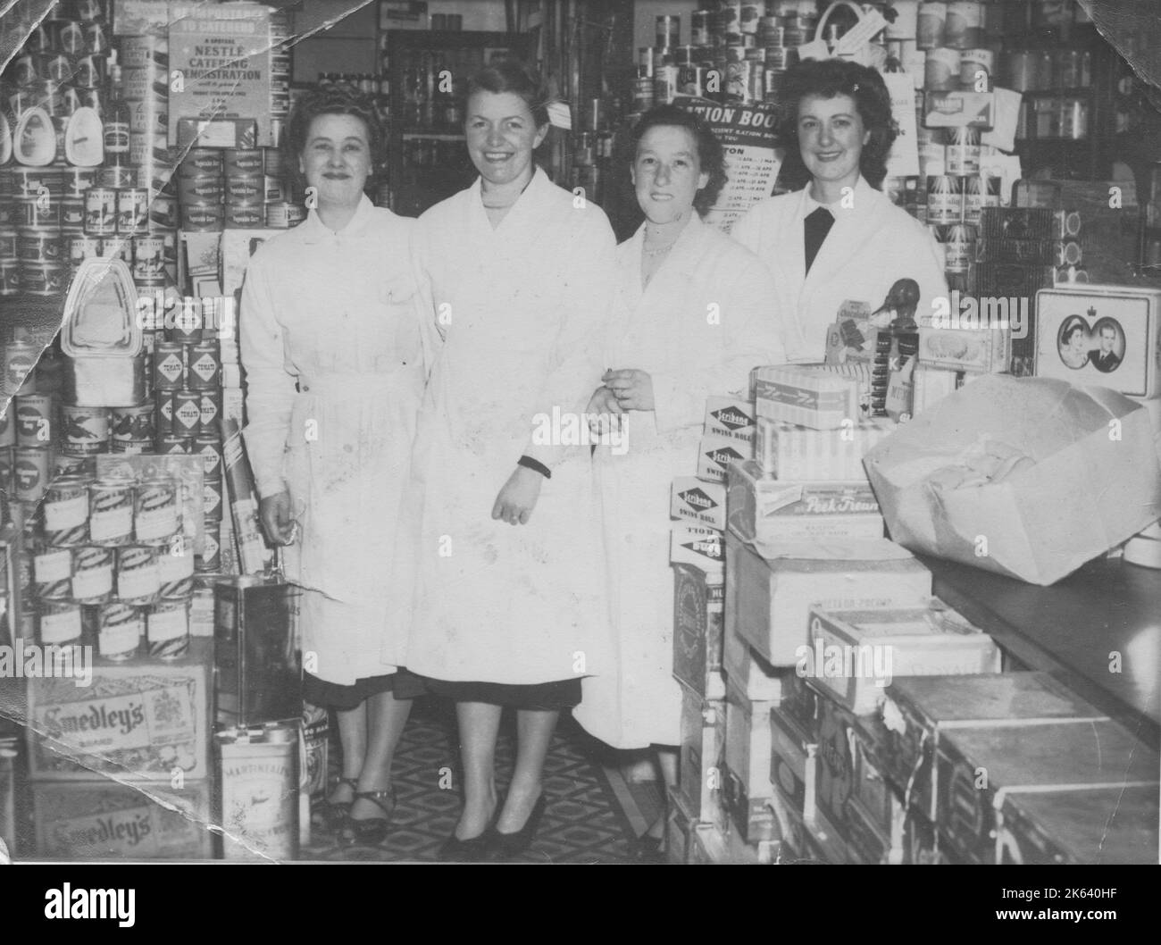 Four shop workers line up for a photograph in a well-stocked grocery store. The rationing sign behind them and the royal tin suggests the photograph dates to around 1952 or 1953 (rationing ended in Britain in 1954). Stock Photo