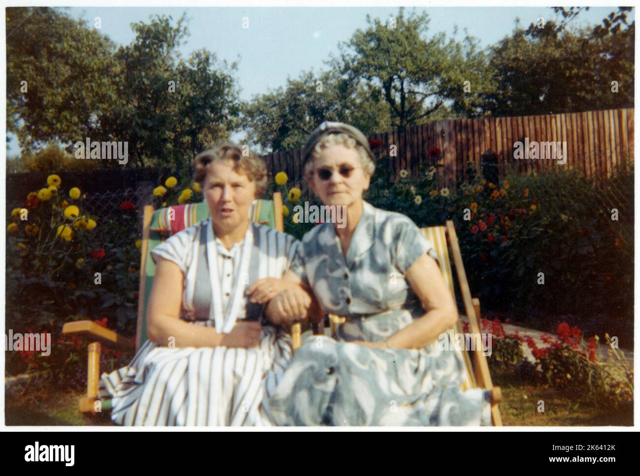 Two older women sitting arm-in-arm in garden chairs in the late afternoon summer light - September, 1959 Stock Photo