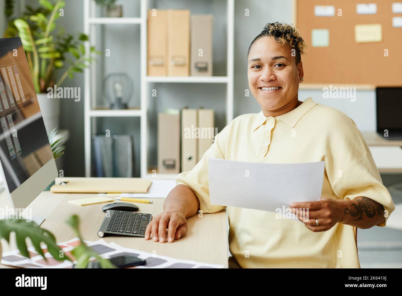 Portrait of tattooed black woman designing websites and mobile apps in office and smiling at camera Stock Photo