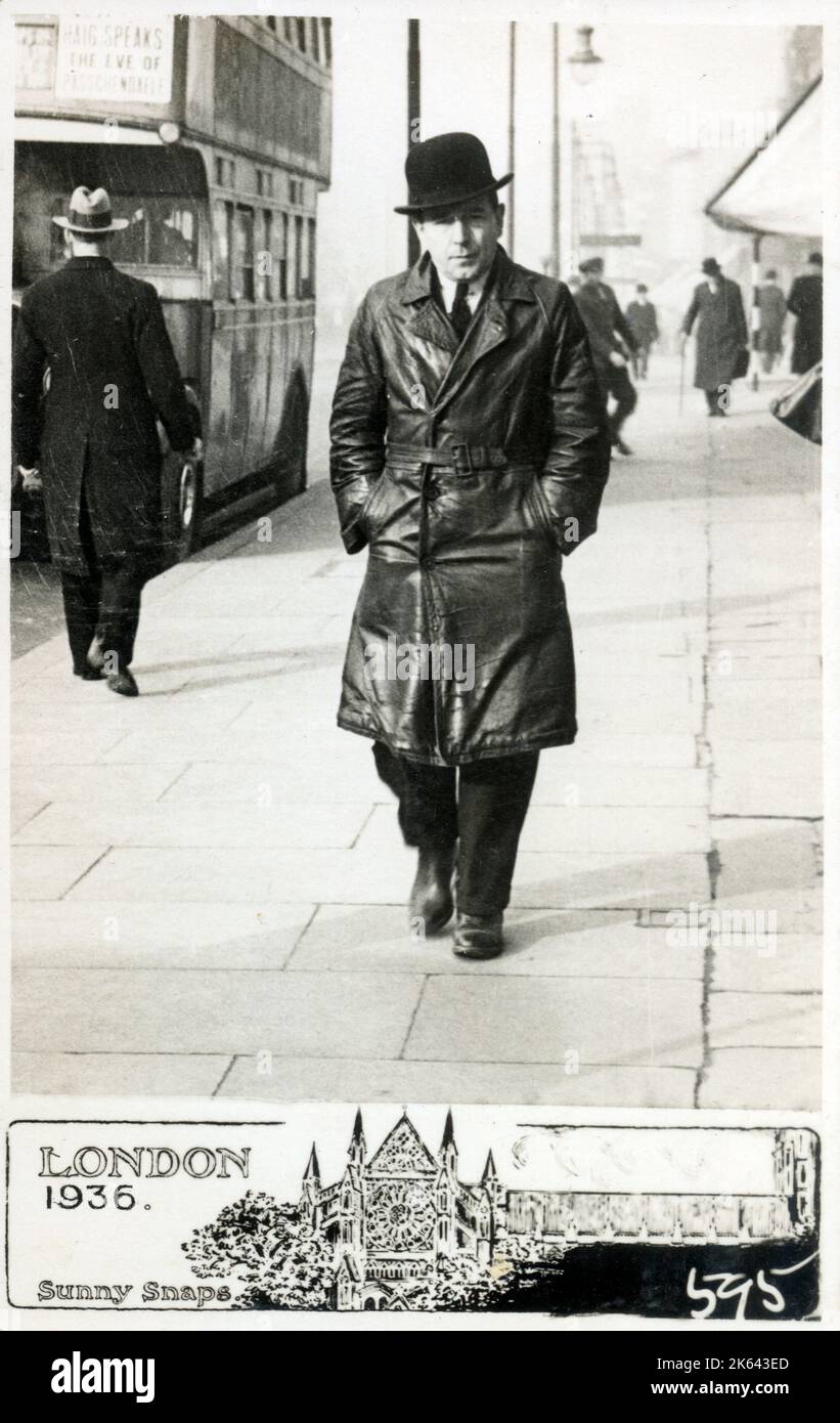 A middle aged businessman in a black leather full length overcoat walking along a London pavement on a cold winter's morning, his hands firmly in his pockets! Stock Photo