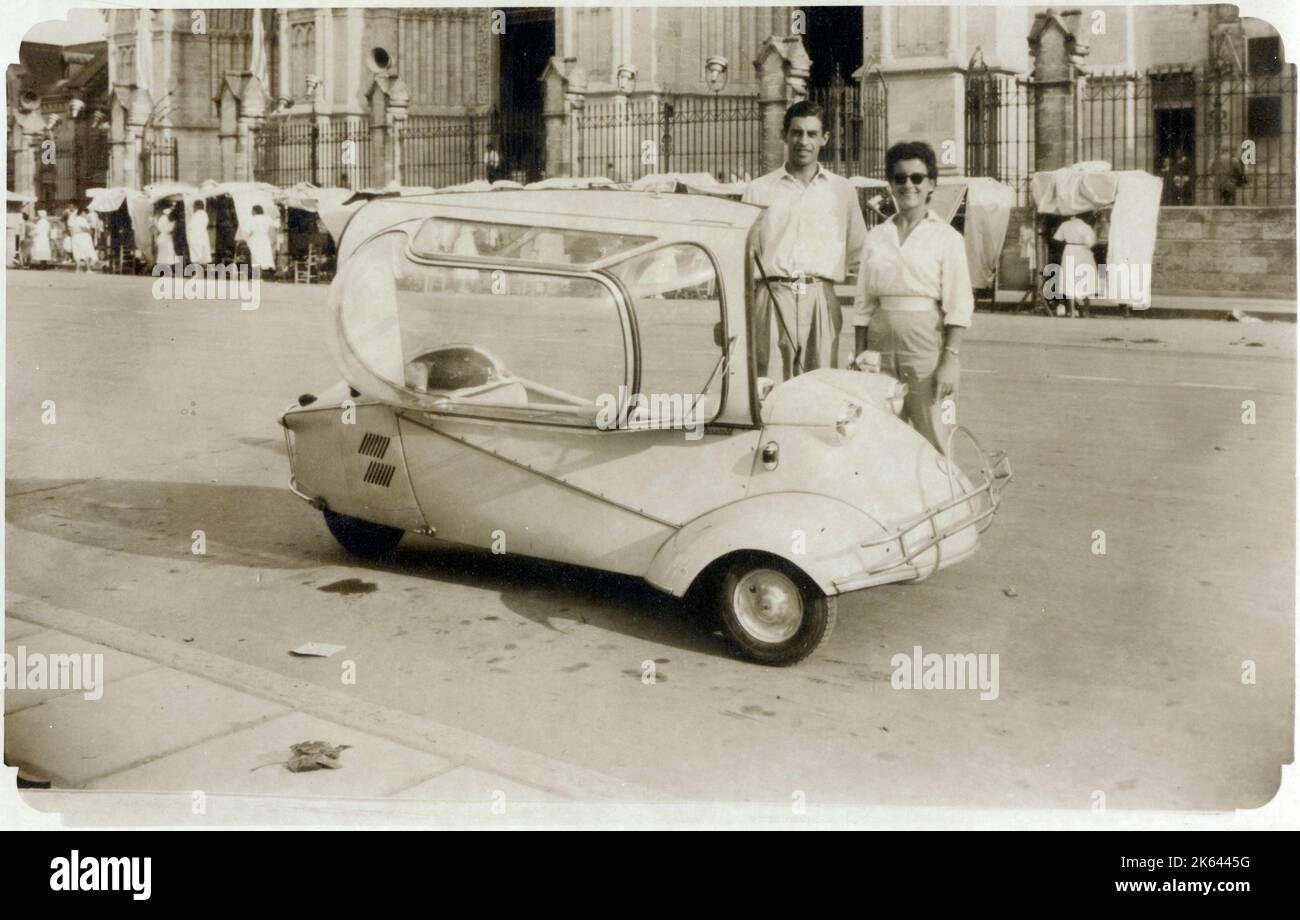 A young (possibly) Italian couple standing proudly next to their Messerschmitt KR200, or Kabinenroller (Cabin Scooter), a three-wheeled bubble car designed by the aircraft engineer Fritz Fend and produced in the factory of the German aircraft manufacturer Messerschmitt from 1955 to 1964. Stock Photo