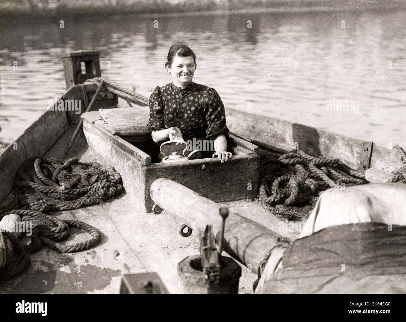 Early 20th century vintage press photograph - family life on board a boat, social history, poverty, England, 1920s - smiling woman boiling a kettle Stock Photo