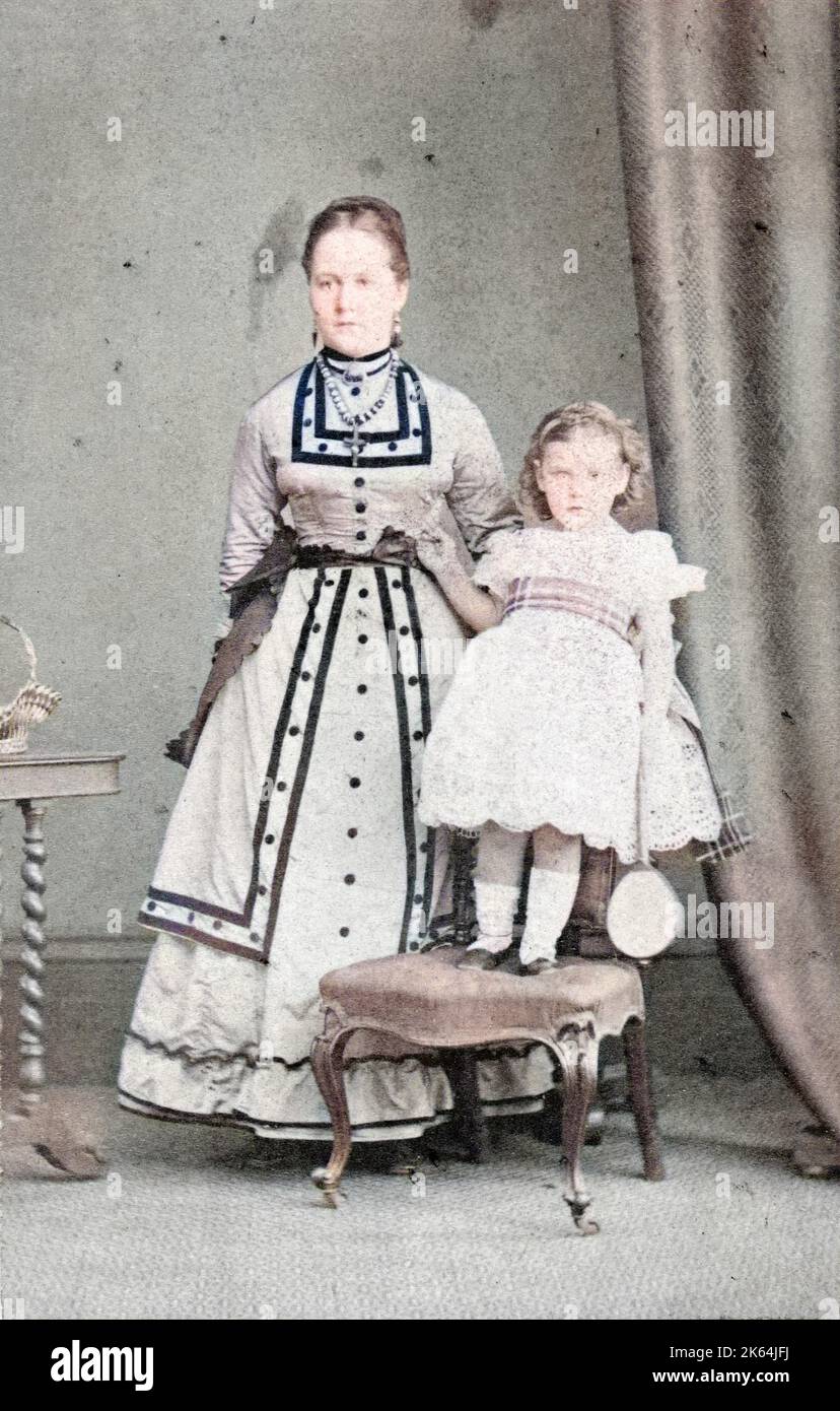 An upper class Victorian girl, Beatrice (Emily Beatrice Violet, d 1930), standing on a chair, with her nanny standing next to her.  They lived at Howbury Hall, Renhold, Bedfordshire. Stock Photo