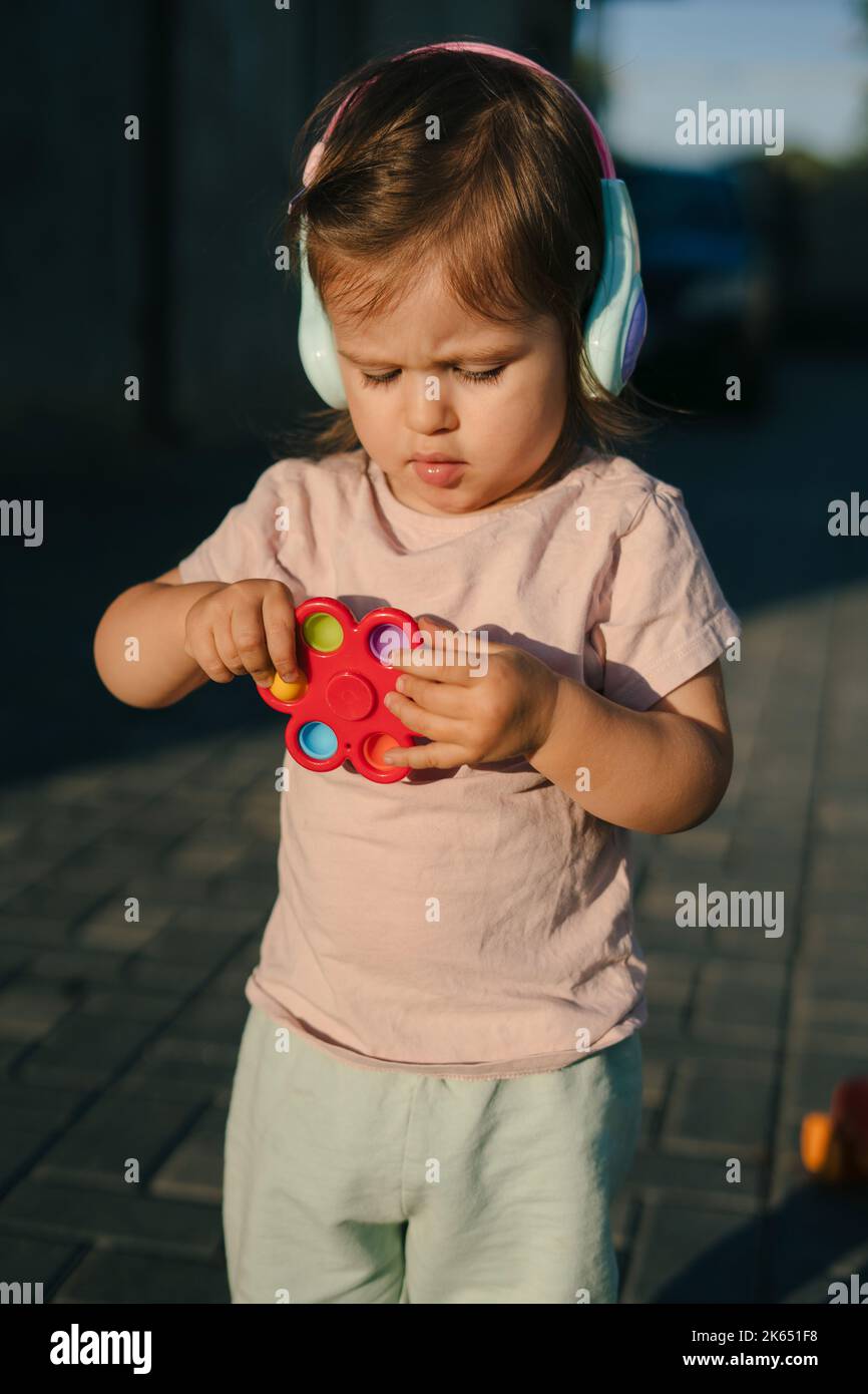 Baby girl standing and holding a toy in her hands, wearing earplugs
