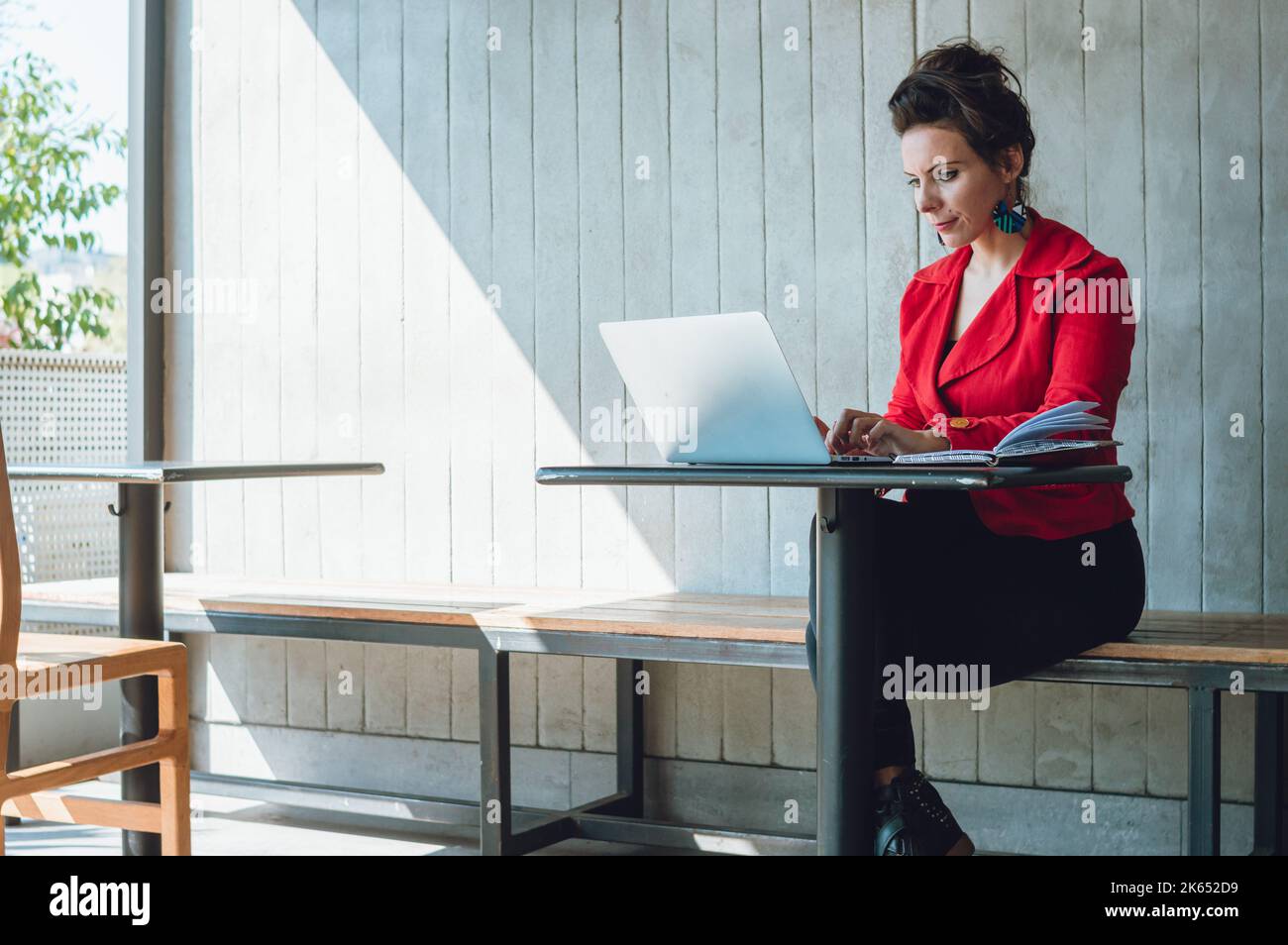 relaxed young caucasian french business woman working on her digital company sitting in a coffee shop, with her laptop and a notepad. Stock Photo