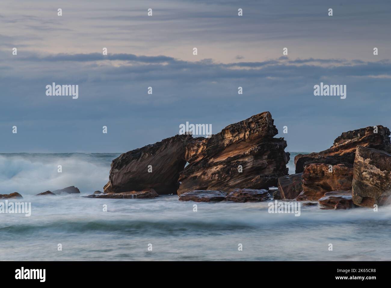 Winter sunrise at the seaside with soft cloud covered sky, rocks and waves rolling in at Killcare Beach on the Central Coast, NSW, Australia. Stock Photo