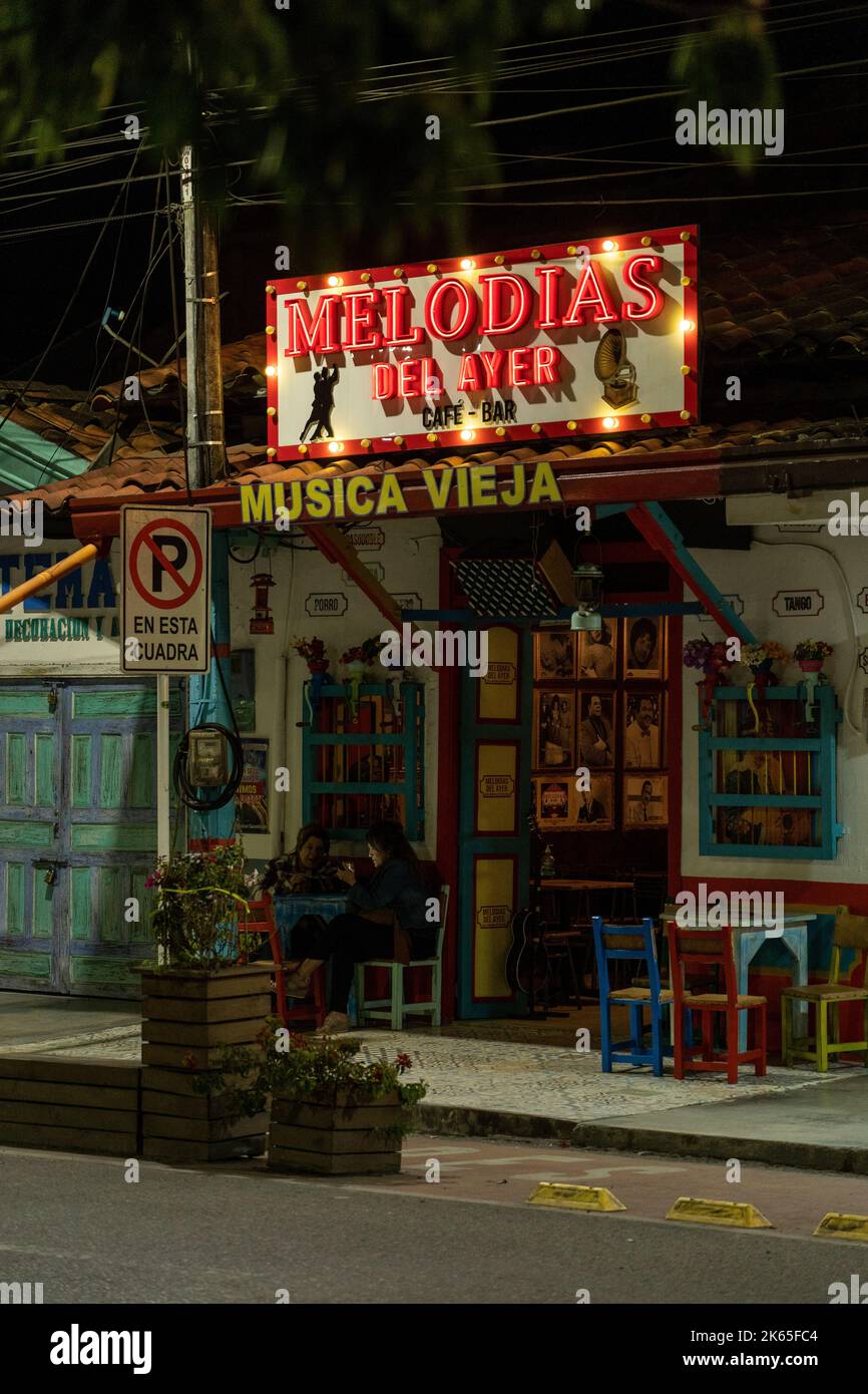 A vertical shot of an illuminated cafe front with old furniture and people chatting, Rionegro,Colombia Stock Photo