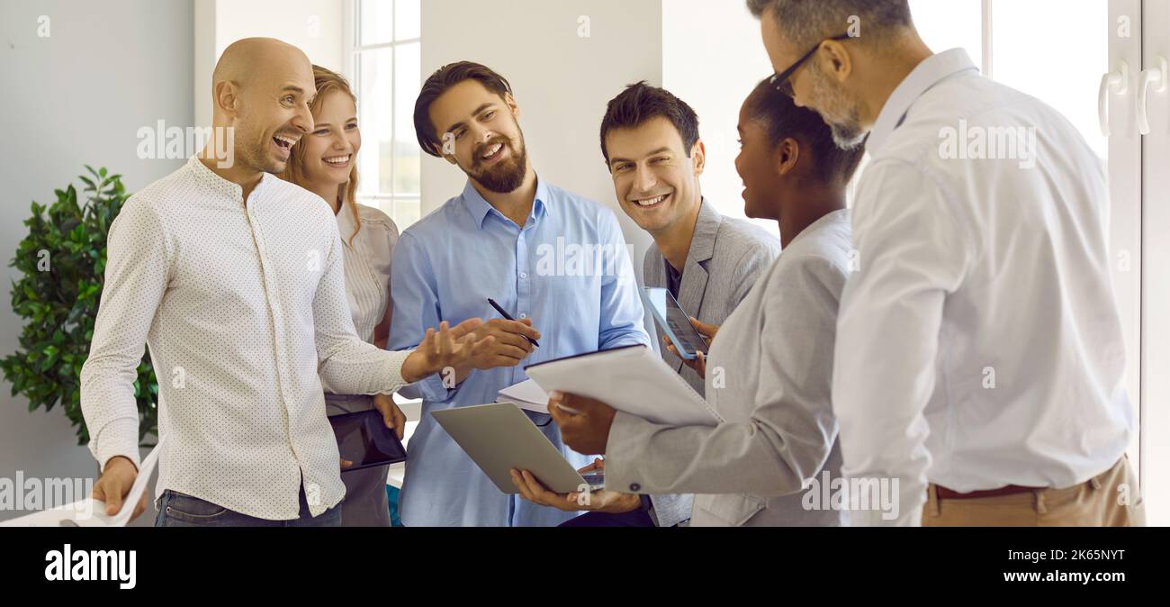 Group of colleagues are talking and joking together while creating and discussing business plan. Stock Photo
