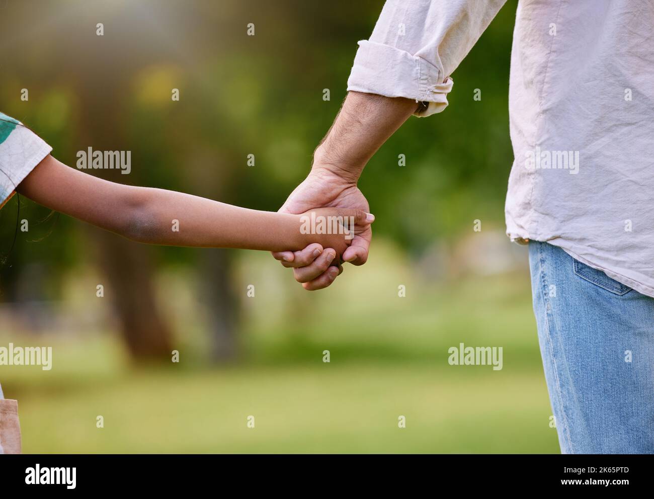 Rearview of a father and daughter holding hands in a park. Mixed race single parent enjoying free time with child outside. Little hispanic girl Stock Photo