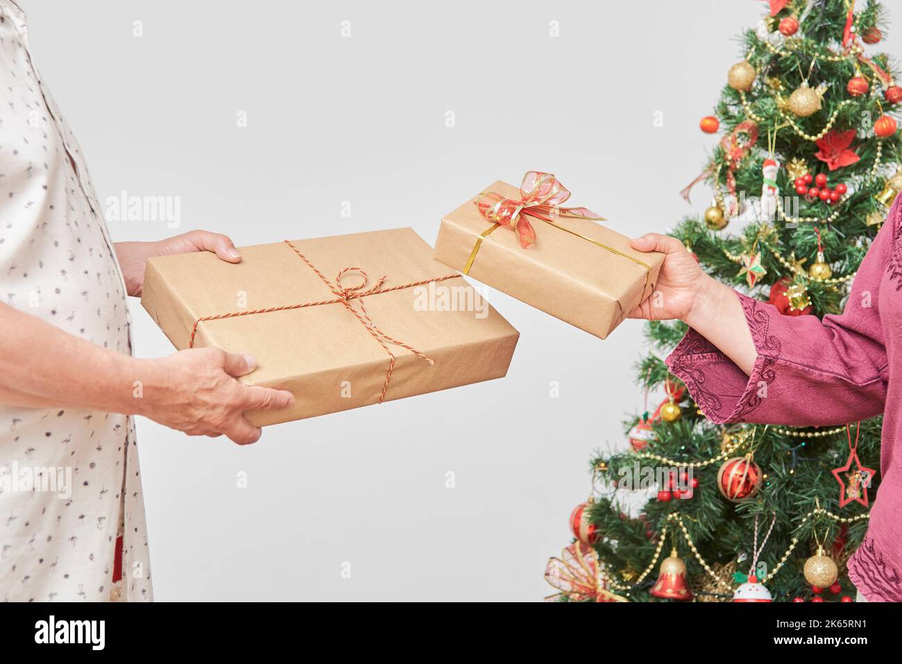 Unrecognizable adult latin couple celebrating the holidays at home together, exchanging Christmas gifts near a decorated tree. Stock Photo