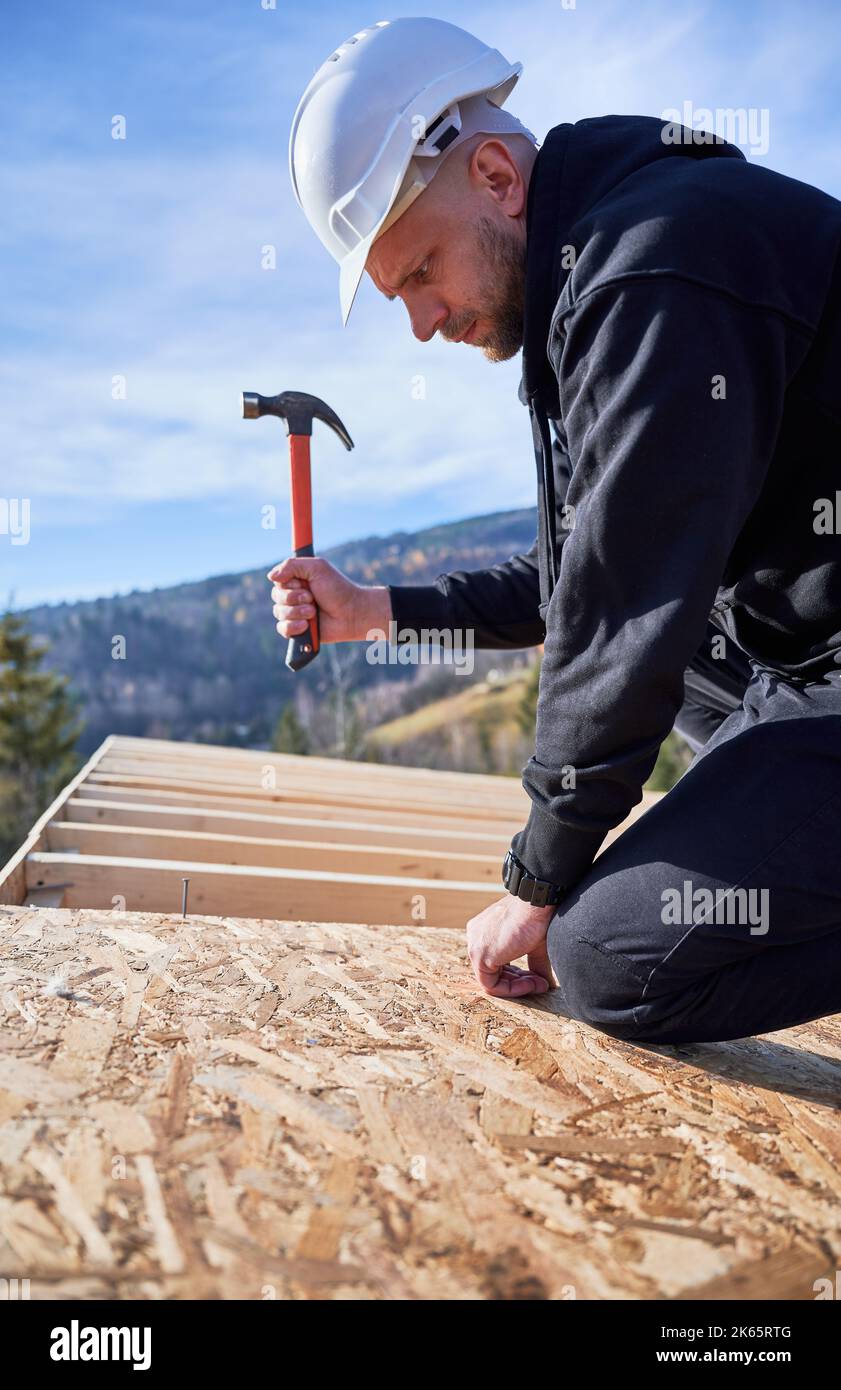 Carpenter hammering nail into OSB panel on the roof top of future