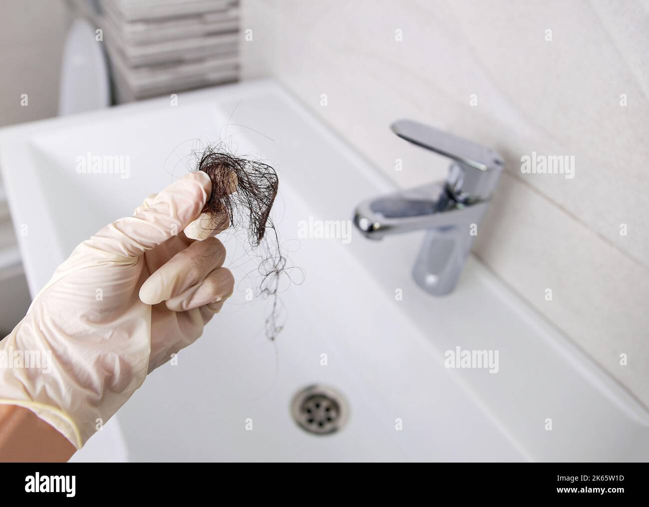Lost hair in sink. A woman cleans the sink from garbage. Selective focus on the hand with hair. Stock Photo