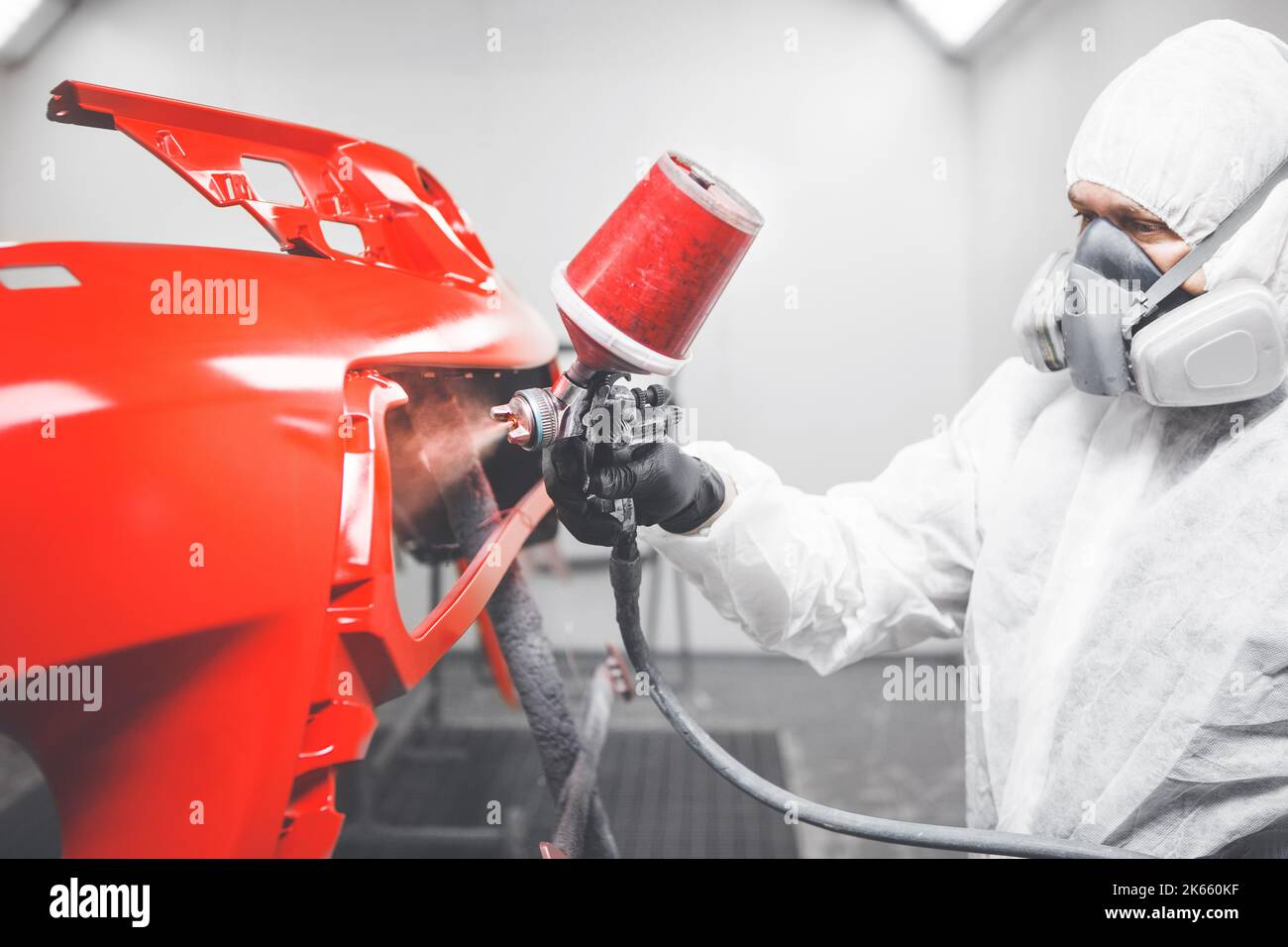 Professional male car painter is painting in garage by airbrush. Man